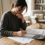 Persona revisando documentos financieros con calculadora en un escritorio de madera