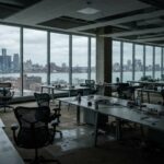 Oficina abierta con escritorios y sillas vacías frente a ventanales con vista a la ciudad