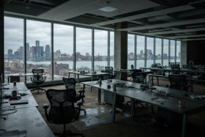 Oficina abierta con escritorios y sillas vacías frente a ventanales con vista a la ciudad